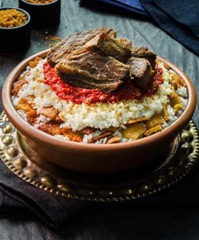 egyptian food of oriental fettah with white rice and crispy bread topped with seasoned garlic sauce crispy fried garlic and veal chunks on rustic dark background