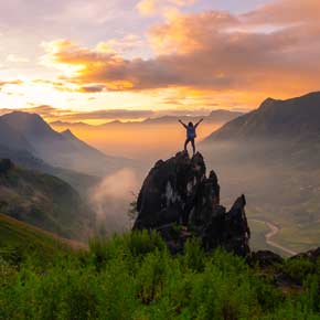 Solo traveler poses infront of a sunset on a rock overlooking the valleys in Sapa